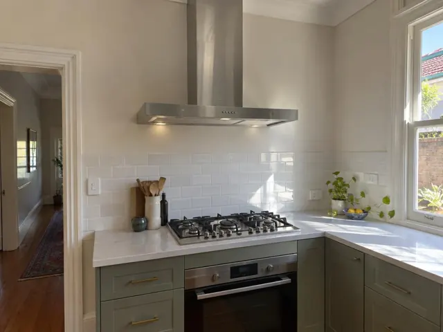 Stainless steel range hood above a gas cooktop in a modern kitchen with white tiled splashback in Ashfield